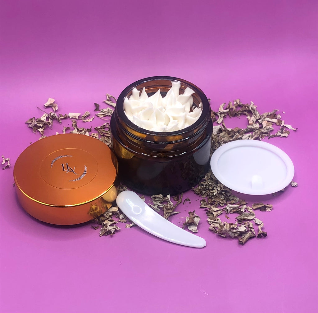 Cosmetic jar with white product, gold lid, and white applicator on a purple background