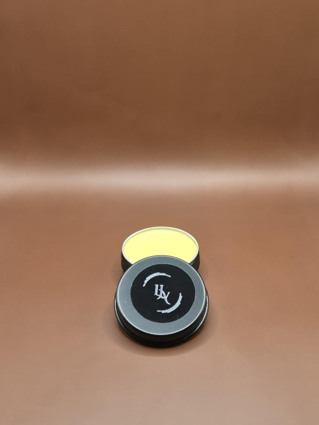 Two small cylindrical containers with black lids on a brown leather surface