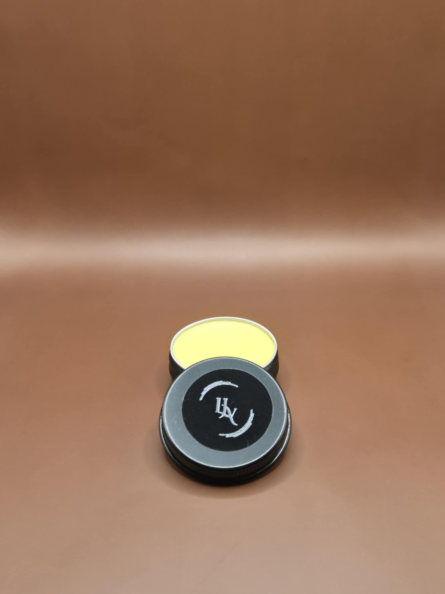 Two small cylindrical containers with black lids on a brown leather surface